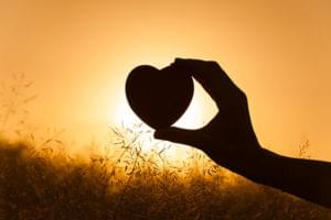A person holding up a heart in front of a sun